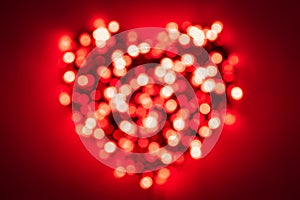 Heavily blurred red lights from a garland forming a heart shape on red background with a vignetting effect