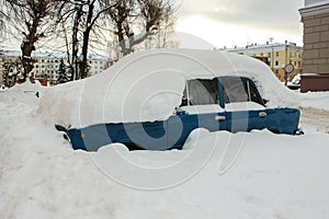 Heavily snow-covered blue retro car parked in the city street