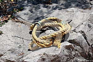 Heavily used dilapidated broken old yellow fishing rope repaired with plastic zip ties and left wrapped on rocky beach