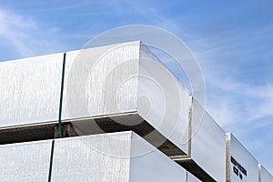 Heavy aluminum bars stacked on top of each other in an aluminum smelting plant, against the blue sky.