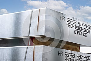 Heavy aluminum bars stacked on top of each other in an aluminum smelting plant, against the blue sky.