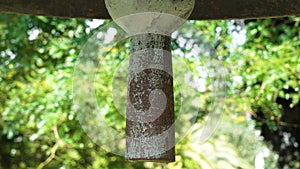 Heavy antique bell clapper against the background of summer foliage of trees.