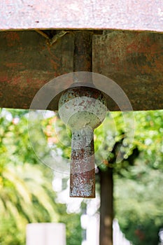 Heavy antique bell clapper against the background of summer foliage of trees