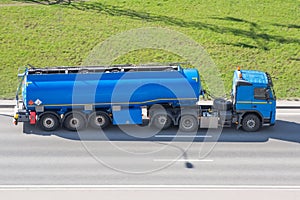 Heavy big fuel tanker with blue lame tank driving on city highway, side aerial view