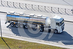 Heavy big fuel tanker with shiny metal lame tank driving on city highway, side aerial view