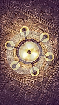 A heavy chandelier with many shades under a stucco ceiling in an old building