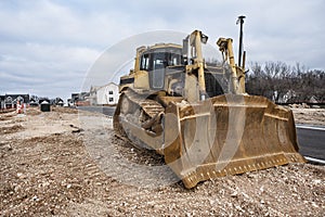 Heavy construction equipment bulldozer on dirt at new home constructions site in subdivision houses in background