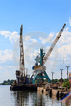 Heavy cranes in cargo port on the riverbank