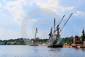 Heavy cranes in cargo port on a riverbank