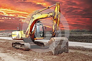 A heavy crawler excavator with a large bucket is getting ready for work against the sunset. Beautiful view of the excavator