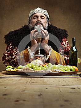 Heavy is the crown. A mature king feasting alone in a banquet hall.