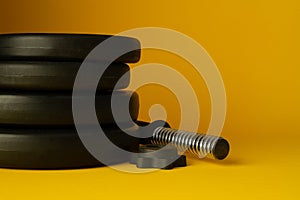 Heavy dumbbells barbell weight plates on yellow background.