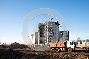 Heavy dump trucks and hydraulic luffing jib tower cranes works at a construction site.