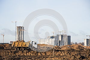 Heavy dump trucks and hydraulic luffing jib tower cranes works at a construction site. Tower crane