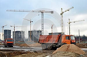 Heavy dump trucks and hydraulic luffing jib tower cranes works at a construction site. Tower crane constructing a new residential