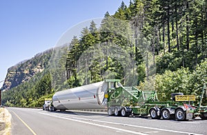 Heavy duty big rig semi truck transporting part of long oversized windmill generator pole on the specialized semi trailer with