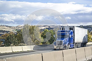 Heavy duty blue big rig semi truck transporting frozen cargo in reefer semi trailer driving on the mountain road in sunny day