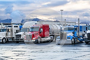 Heavy duty different big rigs semi trucks with loaded semi trailers standing on the truck stop parking lot for truck drivers rest