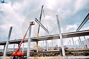 Heavy duty industrial crane operating on construction site, building concrete hall with prefabricated beams