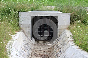 Heavy duty metal bars at local storm drain exit covered with strong metal cover encased in concrete casing leading to stone canal