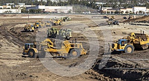 Heavy earthmoving equipment including scapers and motor graders involved in grading operations
