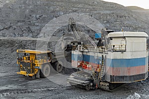 A heavy electric excavator loads ore into a dump truck.