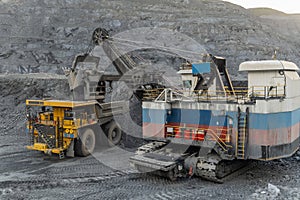 A heavy electric excavator loads ore into a dump truck.