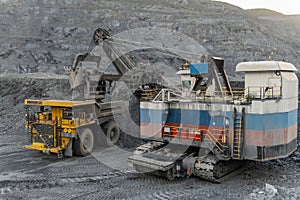 A heavy electric excavator loads ore into a dump truck.