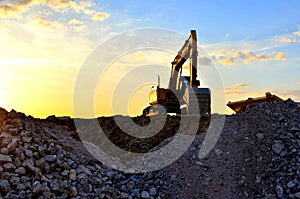 Heavy excavator bucket working in quarry on a background of sunset and blue sky. Mobile jaw stone crusher by the construction site photo