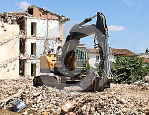 Heavy excavator with a building under demolition on behind