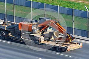 Heavy excavator on transportation truck with long trailer platform on the highway in the city