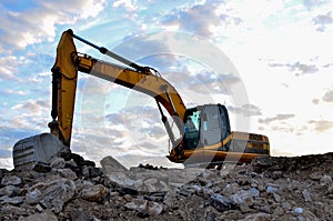 A heavy excavator in a working at granite quarry unloads old concrete stones for crushing and recycling to gravel or cement.