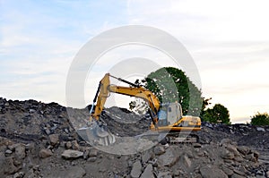 A heavy excavator in a working at granite quarry unloads old concrete stones for crushing and recycling to gravel or cement.