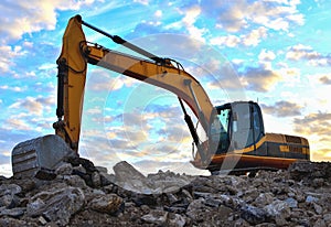 A heavy excavator in a working at granite quarry unloads old concrete stones for crushing and recycling to gravel or cement.