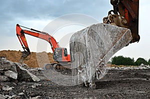 A heavy excavator in a working at granite quarry unloads old concrete stones for crushing and recycling to gravel or cement.