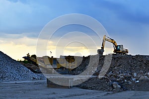 Heavy excavator working in quarry on a background of sunset and blue sky.