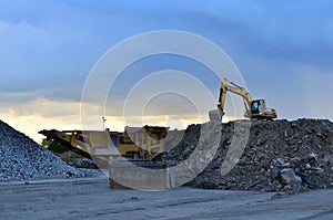 Heavy excavator working in quarry on a background of sunset and blue sky.