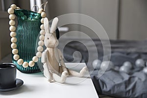 Heavy green glass jug, a wooden hinged rabbit and a cup of coffee are on the bedside table
