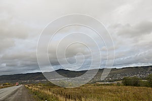 Heavy grey clouds in the cold autumn sky over  village with small houses far away in the mountains and fields. Travelling. People