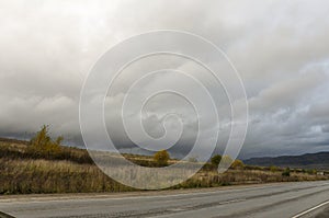 Heavy grey clouds in the cold autumn sky over  village with small houses far away in the mountains and fields. Travelling. People