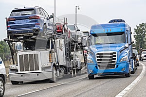 Heavy highway traffic with transporting cars white car hauler big rig semi truck driving side by side with blue semi truck