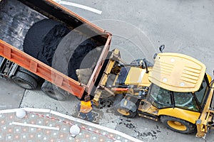 Heavy industrial dump truck unloading hot asphalt .City road construction and renewal site
