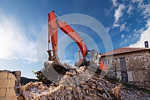 A heavy industrial work machine, digger is destroying an abandoned old building