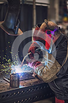 A heavy industrial worker in a factory works with metal on angle grinders while hot sparks are produced as a result.