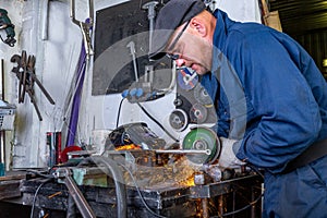 Heavy industry worker cutting steel with angle grinder at car service