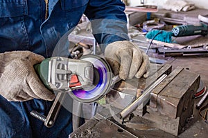 Heavy industry worker cutting steel with angle grinder at car service