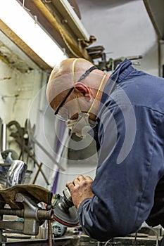 Heavy industry worker cutting steel with angle grinder at car service