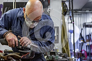 Heavy industry worker cutting steel with angle grinder at car service
