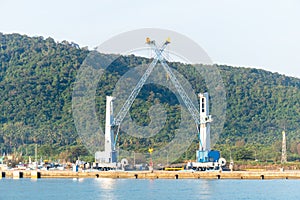 Heavy lifting tower mobile crane for loading cargo in the small commercial sea port with moutain view in the background