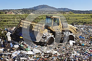 Heavy machinery shredding garbage in an open air landfill. Pollution